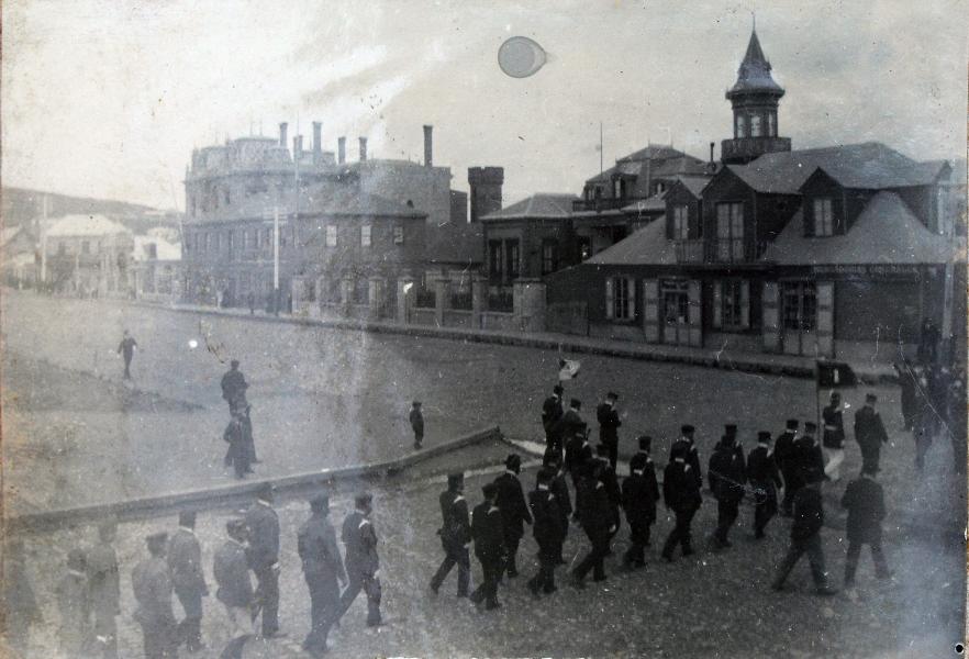 Desfile militar en la esquina de la plaza de Punta Arenas, con construcciones de familias Braun y Menéndez Desfile militar en la esquina de la plaza de Punta Arenas, con construcciones de familias Braun y Menéndez